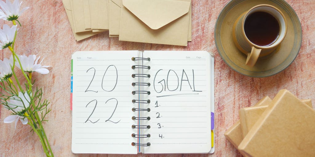 Close-up of a data analyst's desk: a widescreen monitor shows a website analytics dashboard with a sharp, annotated line-chart dip; a hand holds a magnifying glass over the low point while another hand points with a pen. Surrounding items include sticky notes with hypotheses, a timestamped screenshot printout, a steaming coffee cup and a laptop with console logs visible — composition focuses on investigation and urgency.