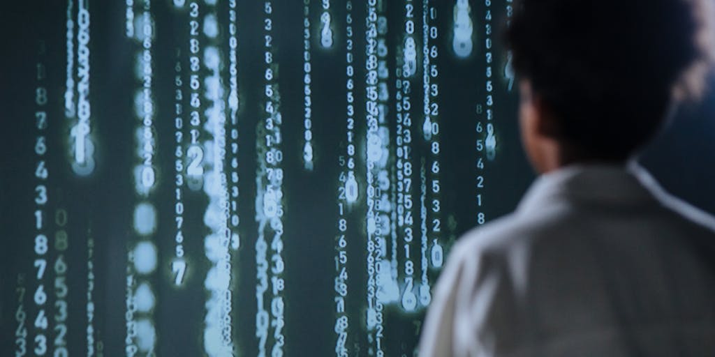 Conceptual, surreal image of a conveyor belt carrying sheets of paper with different paragraphs; above the belt, a scanner machine sprays colored stamps: green 'Human' stamps and red 'AI' stamps. Bits of binary code drift like confetti around the stamping station. Use a slightly desaturated palette with selective color for the stamps to deliver a metaphor for automated content classification.