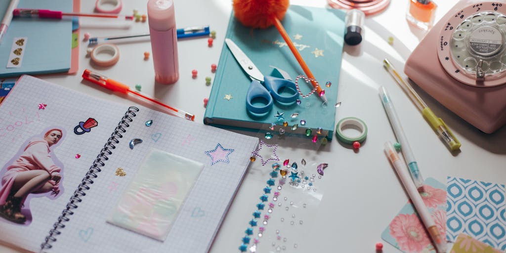 A messy desk strewn with a collage of generic stock photos, torn blog posts, and pixelated images being glued onto a poster board. Large scissors, a glue stick, and yellow price stickers overlay the images; a hand holds a black marker writing repetitive keywords like 'buy now', 'easy', 'viral' to suggest keyword-stuffed, low-effort content.
