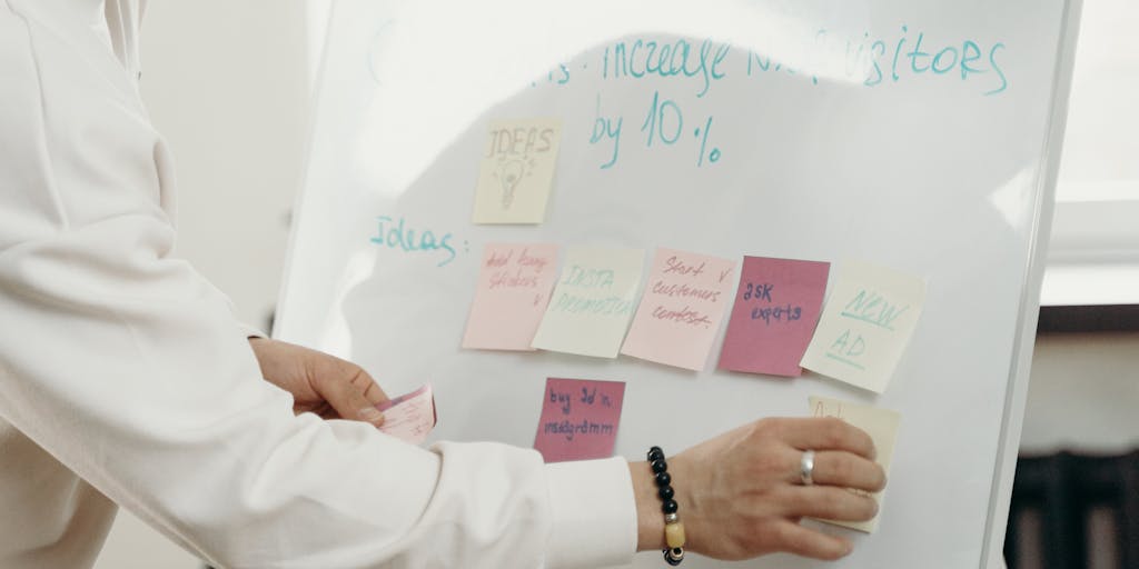 Candid meeting-room photo of a small marketing team in a strategy session: laptops open to analytics dashboards, sticky notes on the table, and a whiteboard behind them filled with hand-drawn funnels, conversion metrics and the word ‘AI’ circled with predictive arrows. Natural, documentary-style lighting captures active discussion and collaborative planning around AI-driven campaigns.