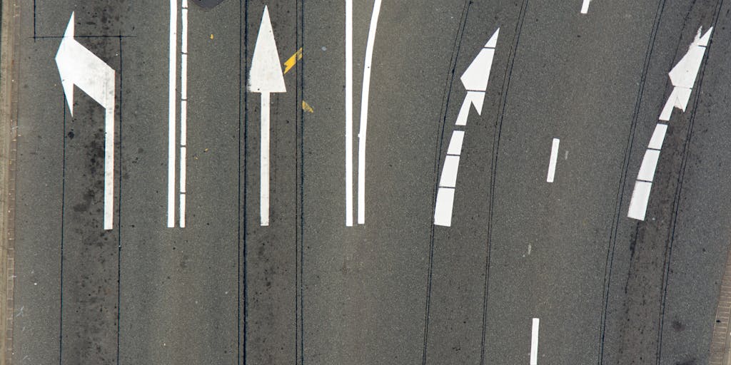 Creative outdoor metaphor: a large highway sign with two oversized arrows — one pointing off the highway (labelled '301') and a newer green arrow being flipped to point back to the original route (labelled '200'). A small silhouette of a person or cyclist at the sign looking relieved. Golden hour lighting to make the scene dramatic and symbolic of changing directions.