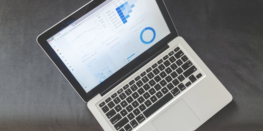 Close-up of a modern workspace with a laptop open to an SEO analytics dashboard showing a prominent 'DR' (Domain Rating) gauge rising from 32 to 55, a line chart of backlinks over time, and colored badge icons for referring domains. Include sticky notes, a coffee cup, and a pair of glasses to set the scene of active analysis.